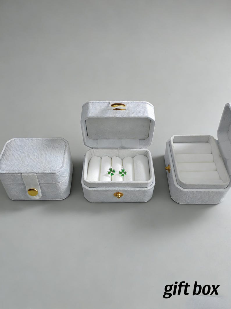 May include: Three white jewelry boxes with gold clasps are displayed. One box is closed, another is open with two green clover earrings inside, and the third is open. The text "gift box" is at the bottom.