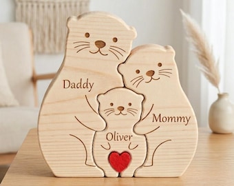 May include: A wooden otter family sculpture with the words "Daddy", "Mommy", and "Oliver" engraved on it. The sculpture features a red heart and is made of light-colored wood. The otters are embracing each other.