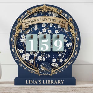 May include: A navy blue wooden book counter with the text "BOOKS READ THIS YEAR" and "LINA'S LIBRARY". The counter displays the number 159 on three light blue flip cards. The design includes floral and bird details.