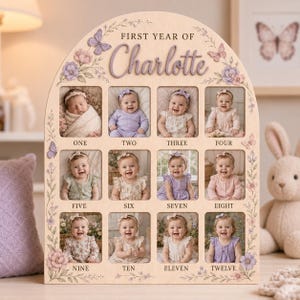Puede incluir: Un tablero de madera arqueado para exhibir fotos titulado FIRST YEAR OF Charlotte, con doce recortes rectangulares para fotos de bebés etiquetados de ONE a TWELVE. El tablero está decorado con ilustraciones de mariposas y flores moradas.