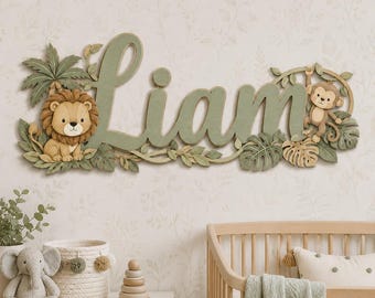 May include: A wall-mounted wooden sign featuring the name LIAM in large, sage green cursive letters. The design is decorated with a cartoon lion on the left, a cartoon monkey on the right, and various green tropical palm leaves and vines.