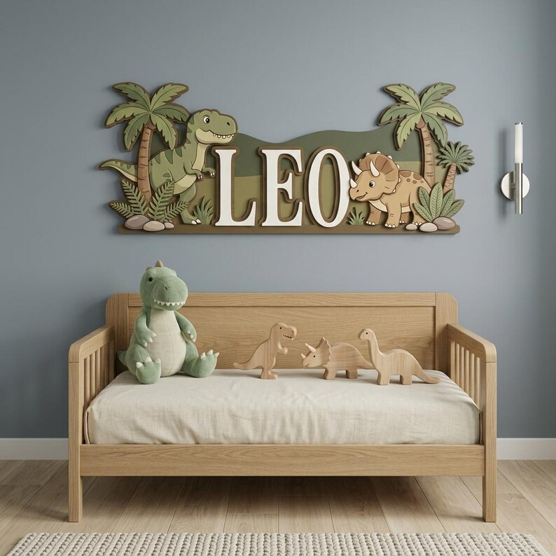 May include: A wooden dinosaur-themed wall decoration with the name "LEO" in white letters. The scene includes a green Tyrannosaurus Rex, a Triceratops, palm trees, and ferns. A plush dinosaur and wooden dinosaur toys are on a wooden bed.