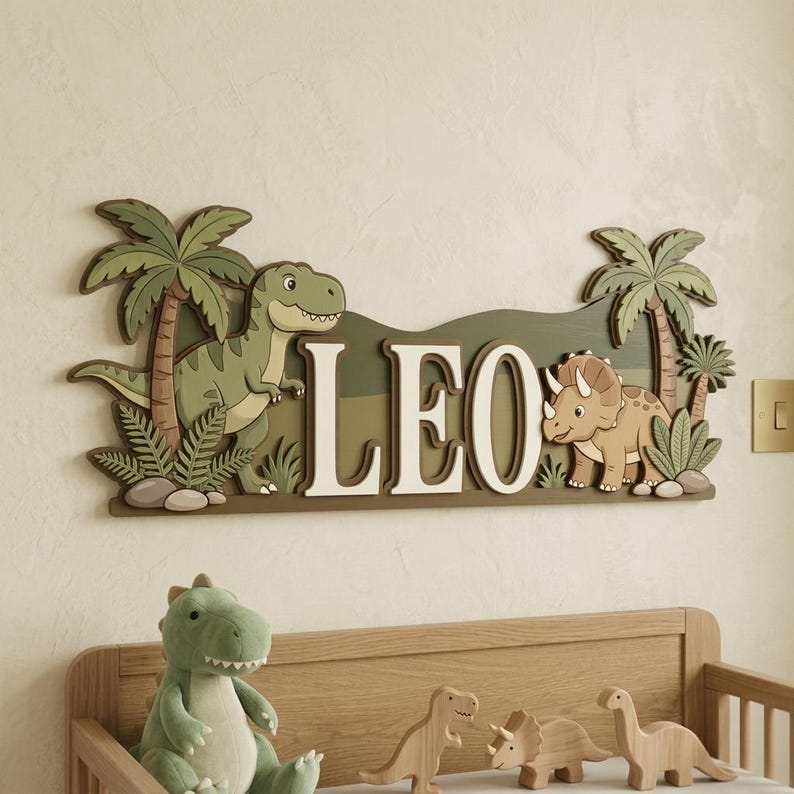 May include: A wooden sign with the name "LEO" in white letters, featuring cartoon dinosaurs and palm trees. The sign is in shades of green and brown, with a T-Rex on the left and a Triceratops on the right. A plush dinosaur and wooden toys are below.