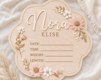 May include: A light wood, scalloped-edge birth announcement sign featuring the name Nora ELISE in white and engraved text. The board includes lines for DATE, TIME, WEIGHT, and LENGTH, decorated with 3D white and soft pink floral accents.
