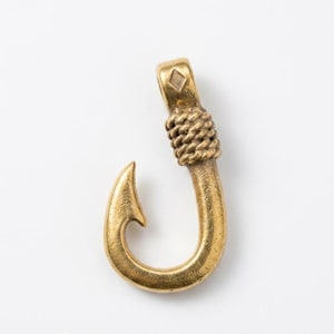 May include: Aureus Anchor pendant in a gold tone. The pendant is shaped like a fish hook with a rope-like detail and a diamond-shaped accent. The text "AUREUS ANCHOR" is below the pendant.
