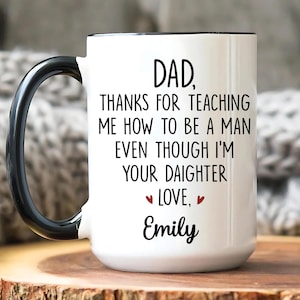 May include: White ceramic mug with a black handle and rim. The mug features the text "DAD, THANKS FOR TEACHING ME HOW TO BE A MAN EVEN THOUGH I'M YOUR DAUGHTER LOVE, Emily" in black script.