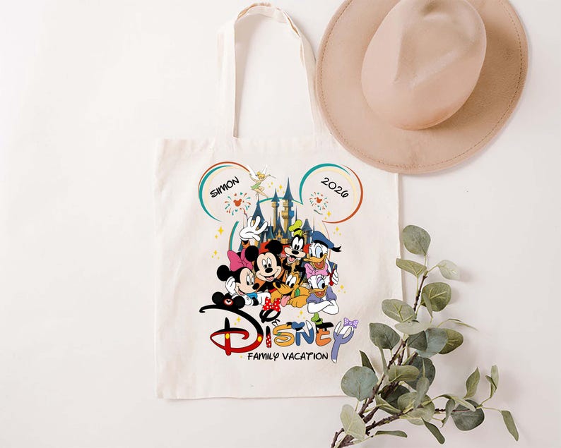 K&ouml;nnte beinhalten: Cremefarbene Tragetasche mit farbenfrohem Disney-Familienurlaubsdesign. Das Design umfasst Micky Maus, Minnie Maus, Donald Duck, Goofy und andere Charaktere. Der Text "Disney Family Vacation" befindet sich darunter.