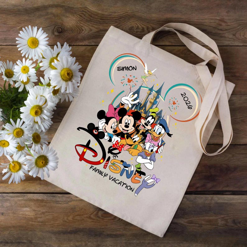 K&ouml;nnte beinhalten: Beige Tragetasche mit einem Disney-Familienurlaubsdesign. Das Design umfasst Micky und Minnie Maus, Donald Duck, Goofy und Daisy Duck. Der Text "Disney Family Vacation" befindet sich unter den Figuren. Das Jahr "2026" ist ebenfalls enthalten.