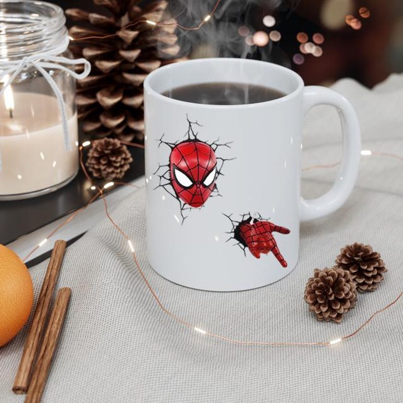 Puede incluir: Taza de cer&aacute;mica blanca con un dise&ntilde;o 3D de la m&aacute;scara y la mano de Spider-Man rompiendo una pared. La taza contiene un l&iacute;quido oscuro. El dise&ntilde;o es rojo y negro.