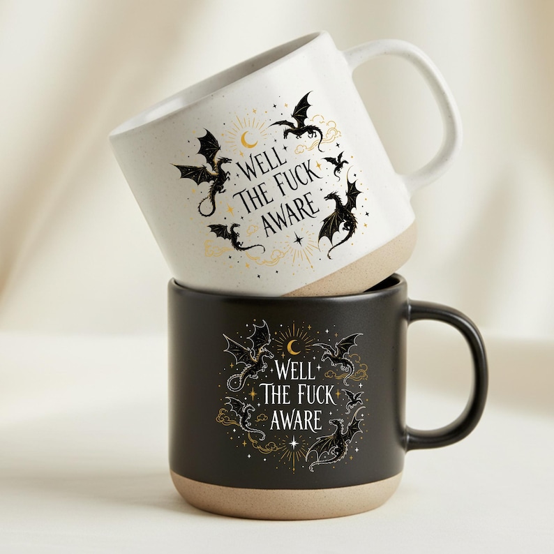 May include: Two ceramic mugs, one white and one black, stacked. Both mugs have a beige base and handle. The mugs feature a dragon design and the text "WELL THE FUCK AWARE". The mugs are designed for hot beverages.