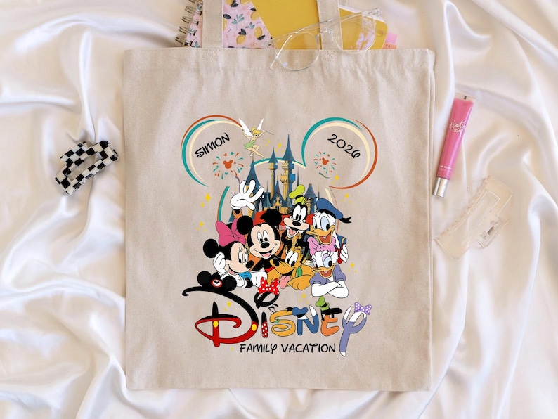 K&ouml;nnte beinhalten: Beige Tragetasche mit einem Disney-Familienurlaubsdesign. Das Design umfasst Micky und Minnie Maus, Goofy, Donald Duck und andere Charaktere. Der Text "SIMON 2026" und "Disney Family Vacation" sind ebenfalls sichtbar.