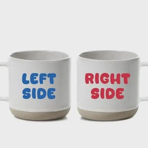 May include: Two white ceramic mugs with a speckled beige base. One mug has the words "LEFT SIDE" in blue, and the other has "RIGHT SIDE" in red. Both mugs have a white handle.