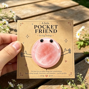 May include: A round, light pink stone with two small black eyes attached to a tan card. The card features the text A little POCKET FRIEND for big feelings and I'm here for you when things feel overwhelming. Take a deep breath, slow down, and remember—you've got this.