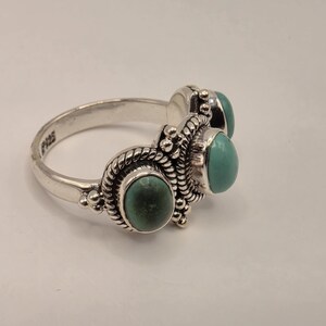 May include: A sterling silver ring featuring three oval-shaped turquoise stones set in decorative rope-textured metal bezels. The band is stamped with 925 to indicate silver purity and displays intricate beaded metalwork surrounding each stone.