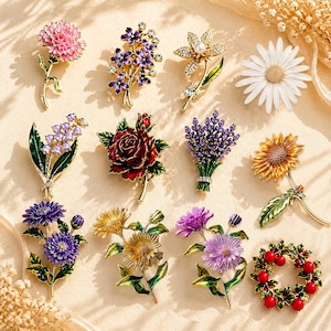 Könnte beinhalten: Eine Sammlung floraler Broschen in verschiedenen Designs. Die Broschen weisen detaillierte Emaillearbeiten auf und umfassen eine rosa Nelke, lila Blumen, eine Gänseblümchen, eine Rose, Lavendel und eine Sonnenblume. Jede Brosche hat ein goldfarbenes Metallfinish.