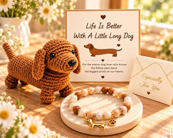 May include: A brown crocheted dachshund figurine, a beaded bracelet with a gold-toned dachshund and paw print charm, and a card with the text "Life Is Better With A Little Long Dog" and "Especially For You" on a small envelope.