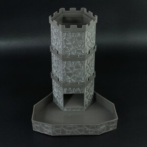 May include: A gray, 3D-printed dice tower with a stone wall design. The tower has a hexagonal top and a tray at the base. The tower is approximately 7 inches tall.