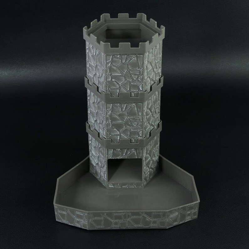 May include: A gray, 3D-printed dice tower with a stone wall design. The tower has a hexagonal top and a tray at the base. The tower is approximately 7 inches tall.
