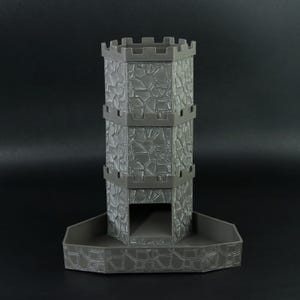 May include: A gray, 3D-printed dice tower shaped like a castle. The tower has a textured stone wall design and a crenelated top. The base is a tray to catch the dice. The tower is approximately 6 inches tall.