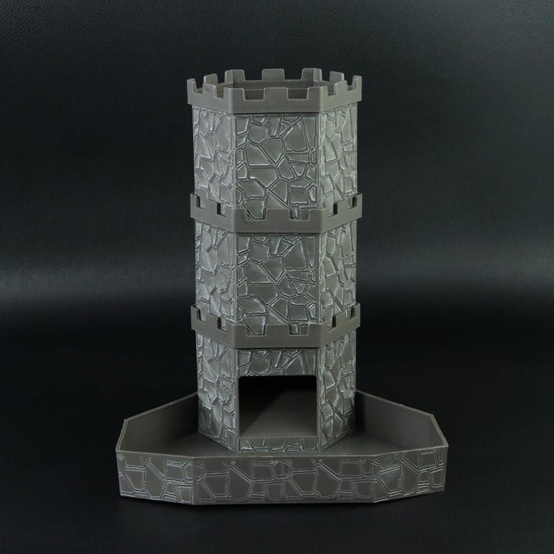 May include: A gray, 3D-printed dice tower shaped like a castle. The tower has a textured stone wall design and a crenelated top. The base is a tray to catch the dice. The tower is approximately 6 inches tall.