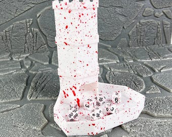 May include: A white dice tower with red splatter details, resembling a castle turret, sits on a matching tray. Several white dice with black numbers are in the tray. The tower is designed for tabletop gaming.