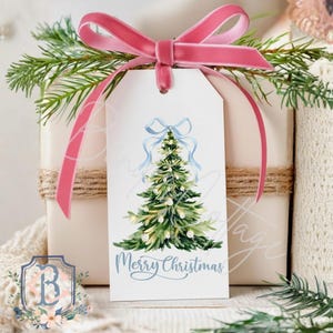 May include: A white gift tag with a watercolor Christmas tree design and the words "Merry Christmas" in light blue script. The tag is adorned with a light blue bow and a pink velvet ribbon. The gift is wrapped in white paper and tied with twine.