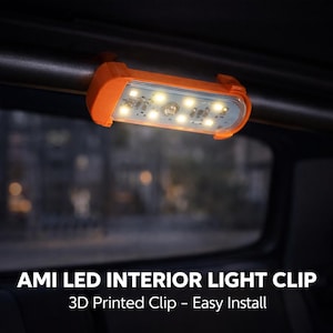 Puede incluir: Un clip naranja impreso en 3D que sujeta una luz interior LED rectangular fijada a una barra horizontal oscura. La luz cuenta con varias bombillas pequeñas y una lente transparente. El texto en la parte inferior dice: AMI LED INTERIOR LIGHT CLIP 3D Printed Clip - Easy Install.