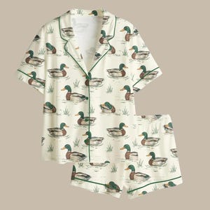 Puede incluir: Conjunto de pijama color crema con un estampado de patos nadando en un estanque. La parte superior de manga corta y los pantalones cortos est&aacute;n ribeteados con ribetes verdes. Los patos est&aacute;n representados en tonos marrones, verdes y blancos.