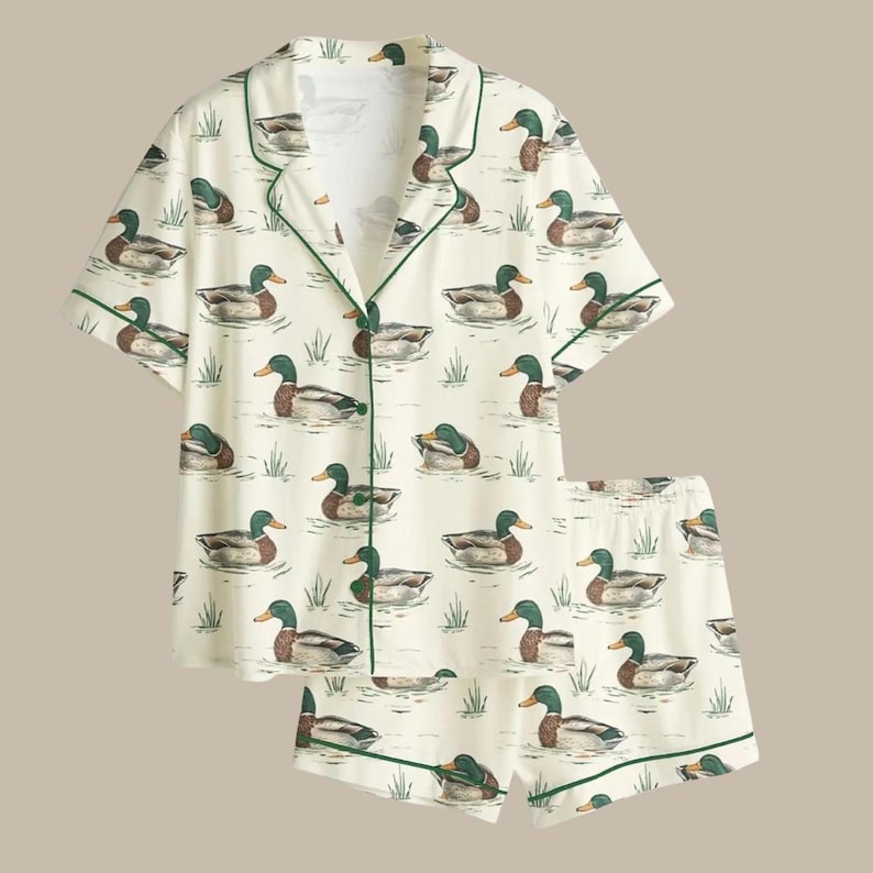 Puede incluir: Conjunto de pijama color crema con un estampado de patos nadando en un estanque. La parte superior de manga corta y los pantalones cortos est&aacute;n ribeteados con ribetes verdes. Los patos est&aacute;n representados en tonos marrones, verdes y blancos.