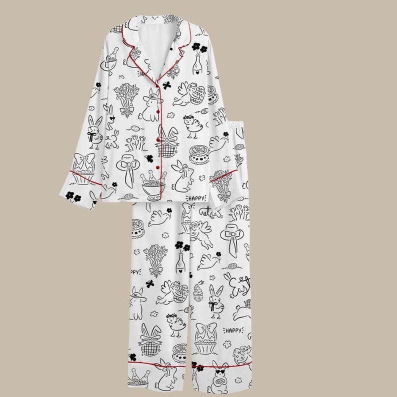 Peut inclure: Ensemble de pyjama blanc avec un motif de dessin anim&eacute; noir et blanc repr&eacute;sentant des lapins, des fleurs et des g&acirc;teaux. L'ensemble comprend un haut boutonn&eacute; et un pantalon, bord&eacute;s d'un passepoil rouge. Le mot "HAPPY" est imprim&eacute; sur le pantalon.