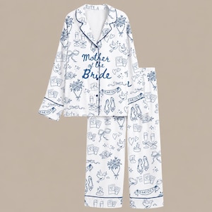 May include: A white pyjama set with long sleeves and long trousers featuring a dark blue line art pattern of flowers, doves, champagne flutes, bows, and shoes. The text Mother of the Bride is printed in dark blue script on the front of the shirt.