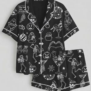 May include: A black pajama set with white piping, featuring a repeating print of skeletons, ghosts, pumpkins, disco balls, and cocktails. The text "She said yes, witches" and "LAST BOO" is printed on the short-sleeved button-down shirt and shorts.