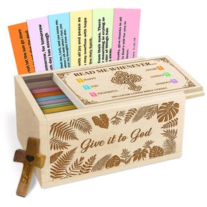 May include: A wooden box with the text "Give it to God" and "Read Me Whenever..." engraved on it. The box contains colorful cards with Bible verses. A wooden cross with the name "Lucas" is also present.