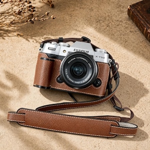 Könnte beinhalten: Eine silberne und schwarze Fujifilm X-T50 Kamera mit einer braunen Lederhülle und passendem Riemen. Das Kameraobjektiv ist schwarz, und der Riemen ist an der Kamera befestigt. Die Hülle hat weiße Nähte.