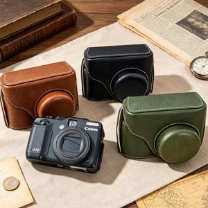 Pode incluir: Uma câmara digital Canon G12 preta posicionada ao lado de três estojos de proteção para câmara em castanho, preto e verde-azeitona. Cada estojo apresenta um acabamento texturado, costuras brancas contrastantes e uma secção arredondada.