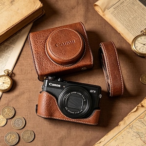 May include: A black Canon G7X digital camera fitted with a brown textured leather case, accompanied by a matching detachable brown leather camera cover and a brown leather strap, all featuring visible stitching and the Canon brand name embossed.