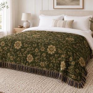 Peut inclure: Une couverture à motifs floraux vert foncé avec une bordure à franges, drapée sur un lit avec une literie blanche. La couverture présente un motif répété de grandes fleurs et de feuillage dans des tons de beige et d'or.