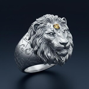 Könnte beinhalten: Silberner Löwenring mit detaillierter Mähne und einem Edelstein auf der Stirn. Der Ring hat ein Himmelsdesign mit Sternen und einem Mond. Kleine Diamanten sind um das Gesicht des Löwen gesetzt.