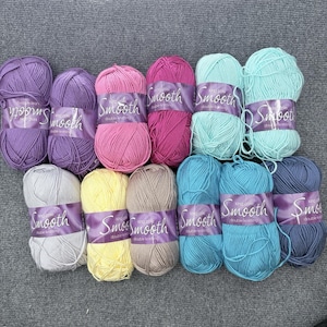 May include: A selection of colourful yarn balls in shades of purple, pink, teal, and blue. Each ball is labelled with the word "Smooth" and "double knitting". Suitable for knitting and crochet projects.
