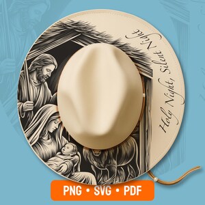 May include: A beige fedora hat featuring a black and white illustration of a nativity scene with figures and the text Holy Night, Silent Night printed along the brim. The hat has a structured crown and a wide brim with a thin brown chin strap.