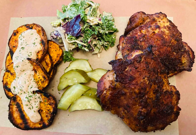 May include: A plate of food with two pieces of roasted chicken, sweet potato fries with a white sauce, a side salad with kale and a creamy dressing, and sliced pickles.