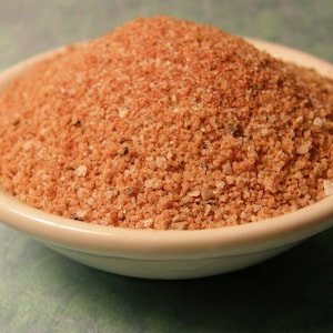 May include: A white bowl filled with a brown and orange spice blend.