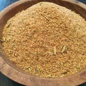 Puede incluir: Primer plano de un cuenco de madera lleno de una mezcla de especias marrones. La mezcla de especias contiene hierbas y otros ingredientes.