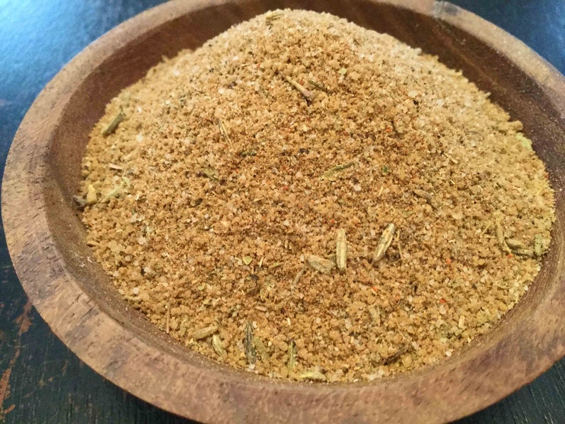 Puede incluir: Primer plano de un cuenco de madera lleno de una mezcla de especias marrones. La mezcla de especias contiene hierbas y otros ingredientes.
