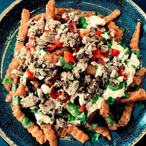 Puede incluir: Un plato de patatas fritas crujientes cubiertas con carne picada, tomates picados, hierbas frescas y una salsa blanca cremosa.