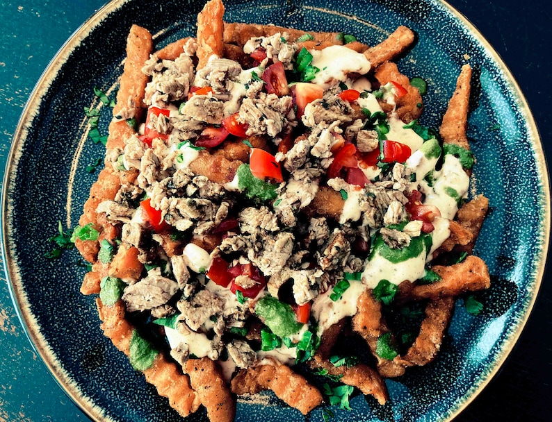 Puede incluir: Un plato de patatas fritas crujientes cubiertas con carne picada, tomates picados, hierbas frescas y una salsa blanca cremosa.