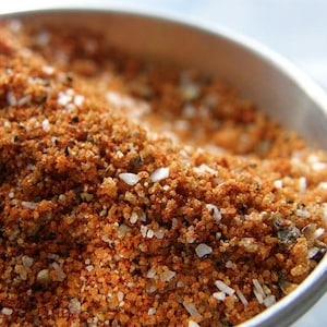 May include: Close-up of a bowl filled with a blend of spices, including red pepper flakes, salt, and black pepper.