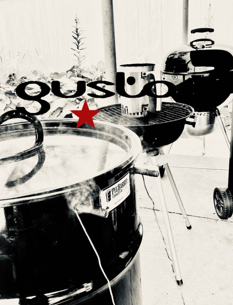 May include: A black metal smoker with a red star and the text "Pig Bar-B-Que Cooker Co." on the side. The smoker is on a tripod stand and there is a black grill in the background.