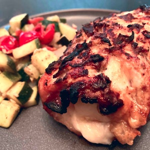 Puede incluir: Primer plano de una pechuga de pollo asada rellena de queso y servida con un acompa&ntilde;amiento de calabac&iacute;n y tomates salteados.