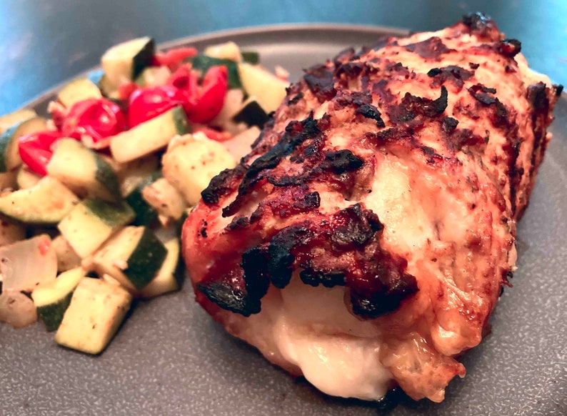 Puede incluir: Primer plano de una pechuga de pollo asada rellena de queso y servida con un acompa&ntilde;amiento de calabac&iacute;n y tomates salteados.